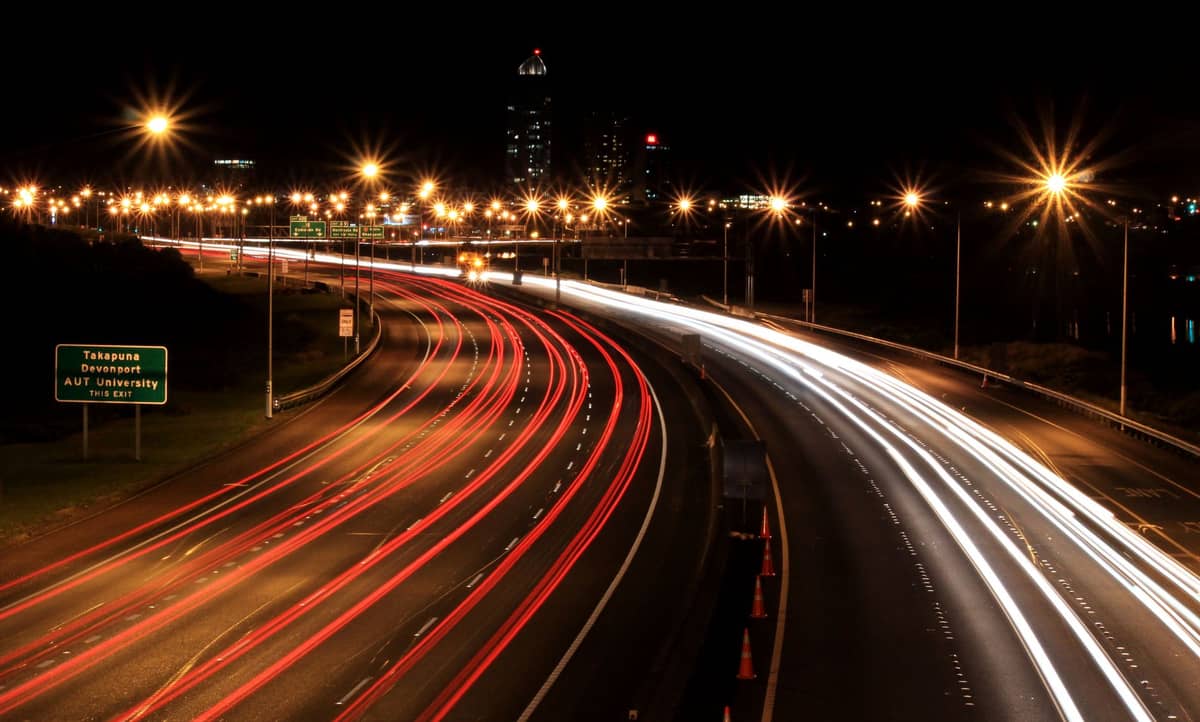 Auckland-Autobahn bei Nacht mit Lichtspuren von Autos und einem Straßenschild nach Takapuna, das eine echte Straßenszene in Auckland zeigt, die für Reisende relevant ist.