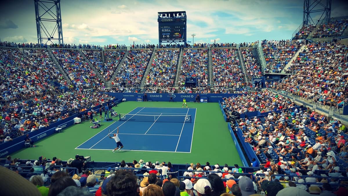 Ein vollgepacktes Tennisstadion voller Zuschauer, die unter einem teilweise bewölkten Himmel ein intensives Match verfolgen und die Aufregung eines Grand-Slam-Events zeigen.