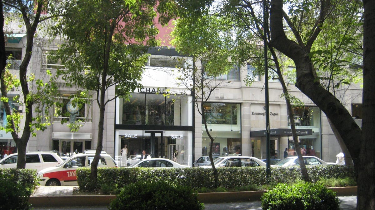 Avenida Presidente Masaryk fiancheggiata da boutique di lusso e alberi frondosi, con marciapiedi affollati, auto parcheggiate e pedoni in un pomeriggio soleggiato.