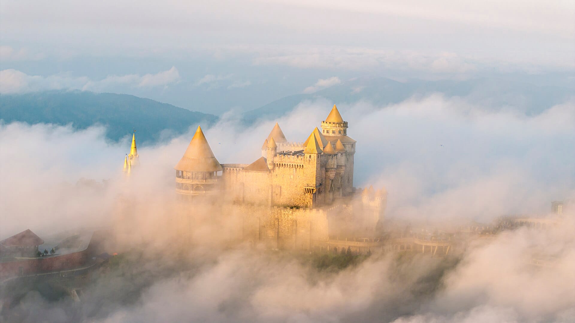 หอคอยปราสาทของหมู่บ้านฝรั่งเศส Ba Na Hills โผล่พ้นเมฆหนาทึบพร้อมภูเขาเป็นฉากหลังในยามรุ่งอรุณ