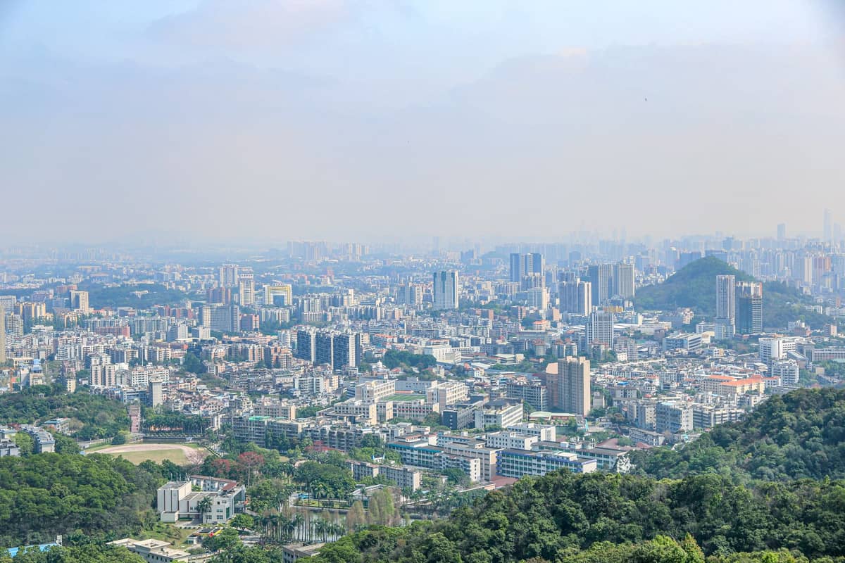 Wide view over Baiyun District, showing residential neighborhoods, urban streets, and forested hills from an elevated vantage point.