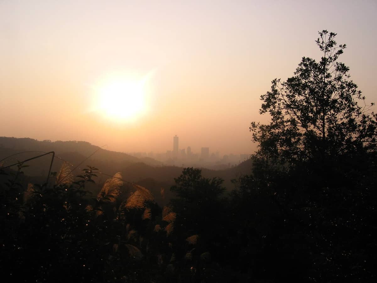 Sunrise over Baiyun Mountain with trees in the foreground, city skyline and hazy buildings visible in the distance.