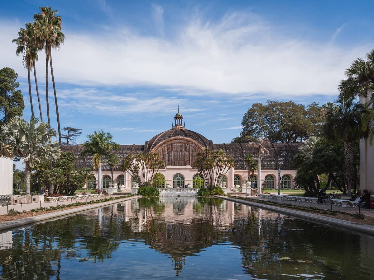 Das Botanical Building im Balboa Park spiegelt sich im ruhigen Lily Pond, umgeben von Palmen und üppigem Grün unter einem blauen Himmel.
