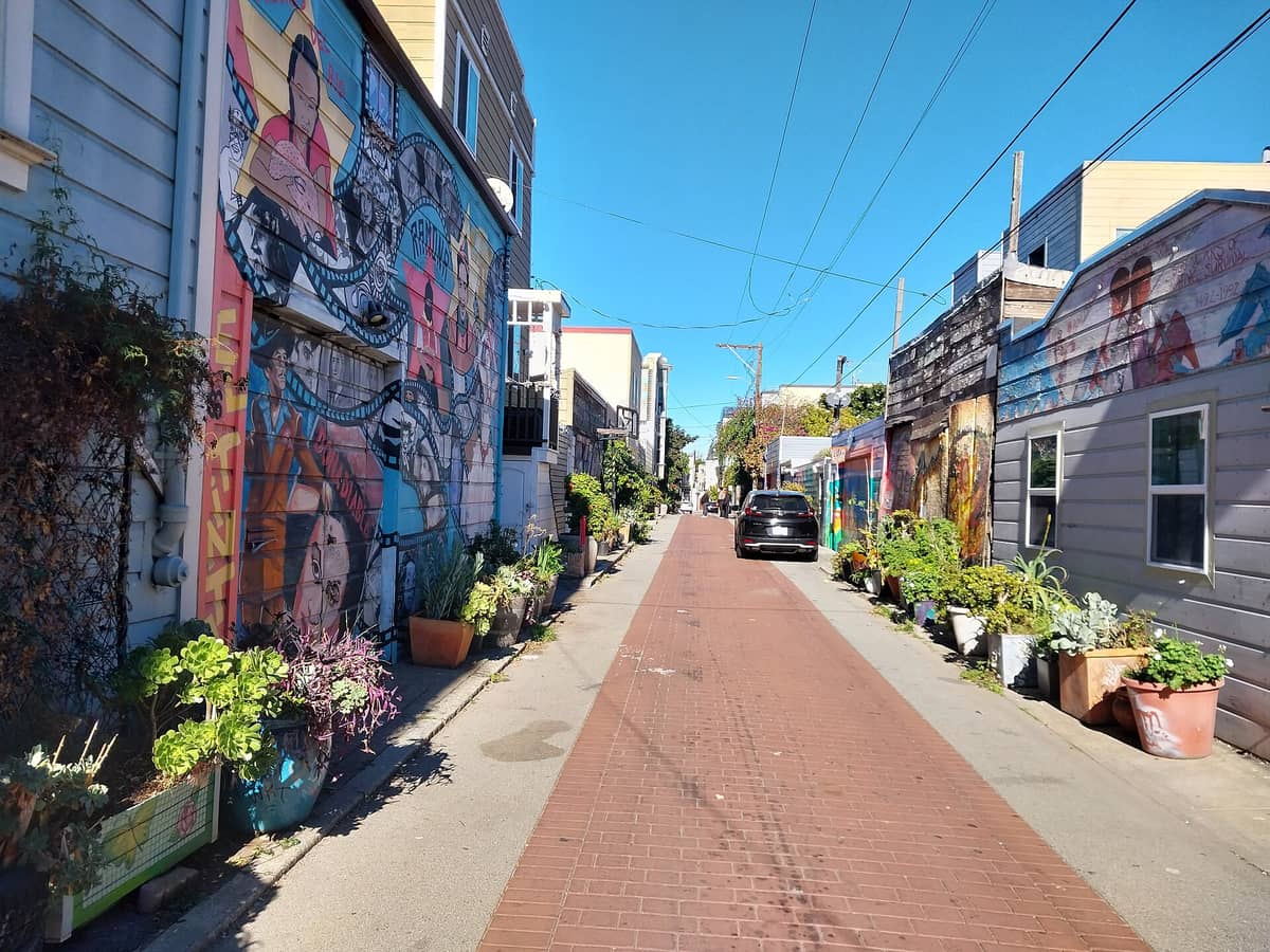 Balmy Alley en el barrio Mission de San Francisco, con vibrantes murales políticos cubriendo ambos lados del estrecho callejón, plantas y un auto estacionado sobre el pavimento de ladrillo.