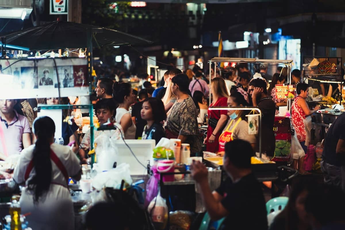 Mercado noturno movimentado em Bangkok com barracas de comida e multidão comendo e explorando vendedores de rua