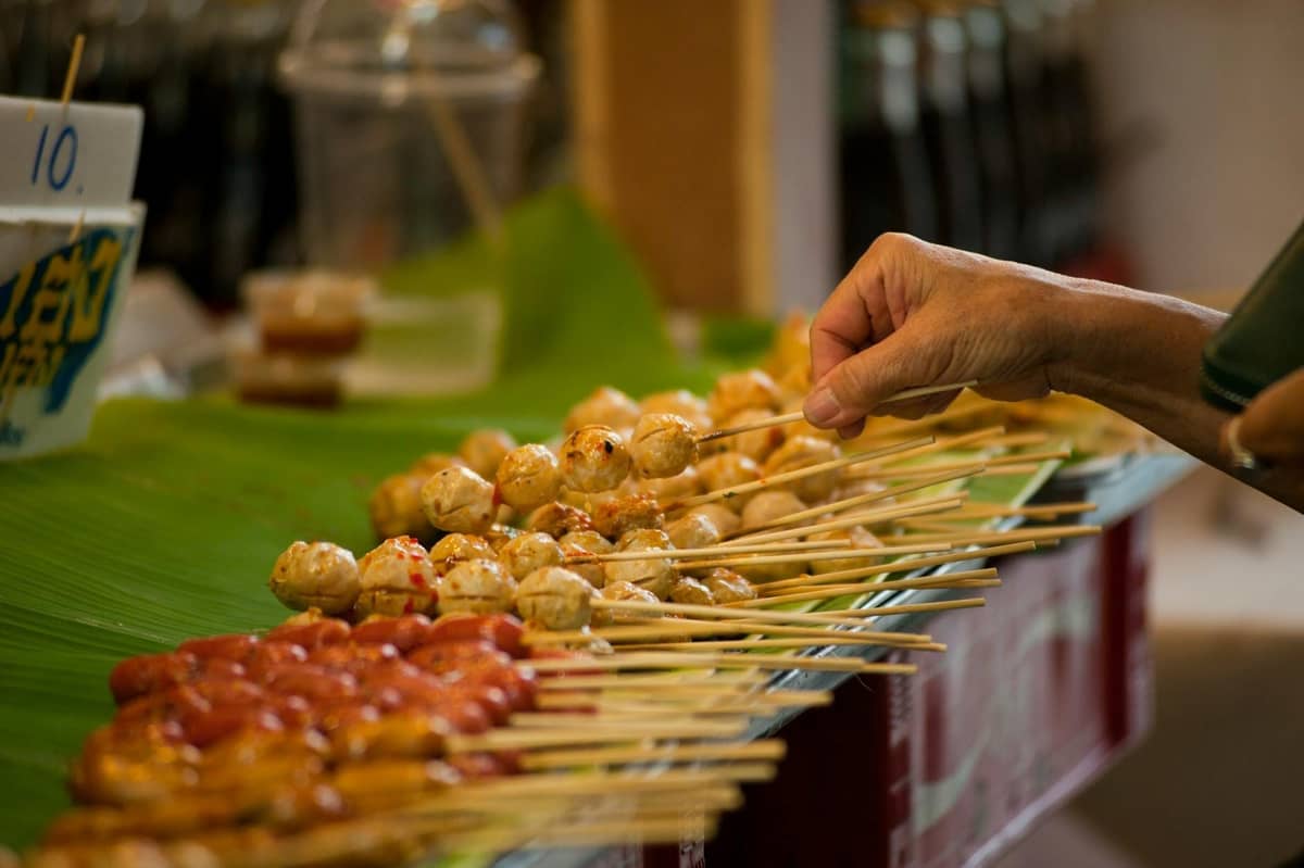 Espetinhos tailandeses grelhados, com almôndegas e salsichas, num mercado noturno de Bangkok