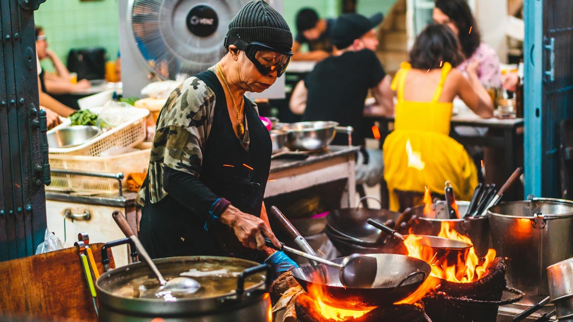 Vendedor de comida de rua cozinhando com wok sobre chamas em mercado noturno de Bangkok