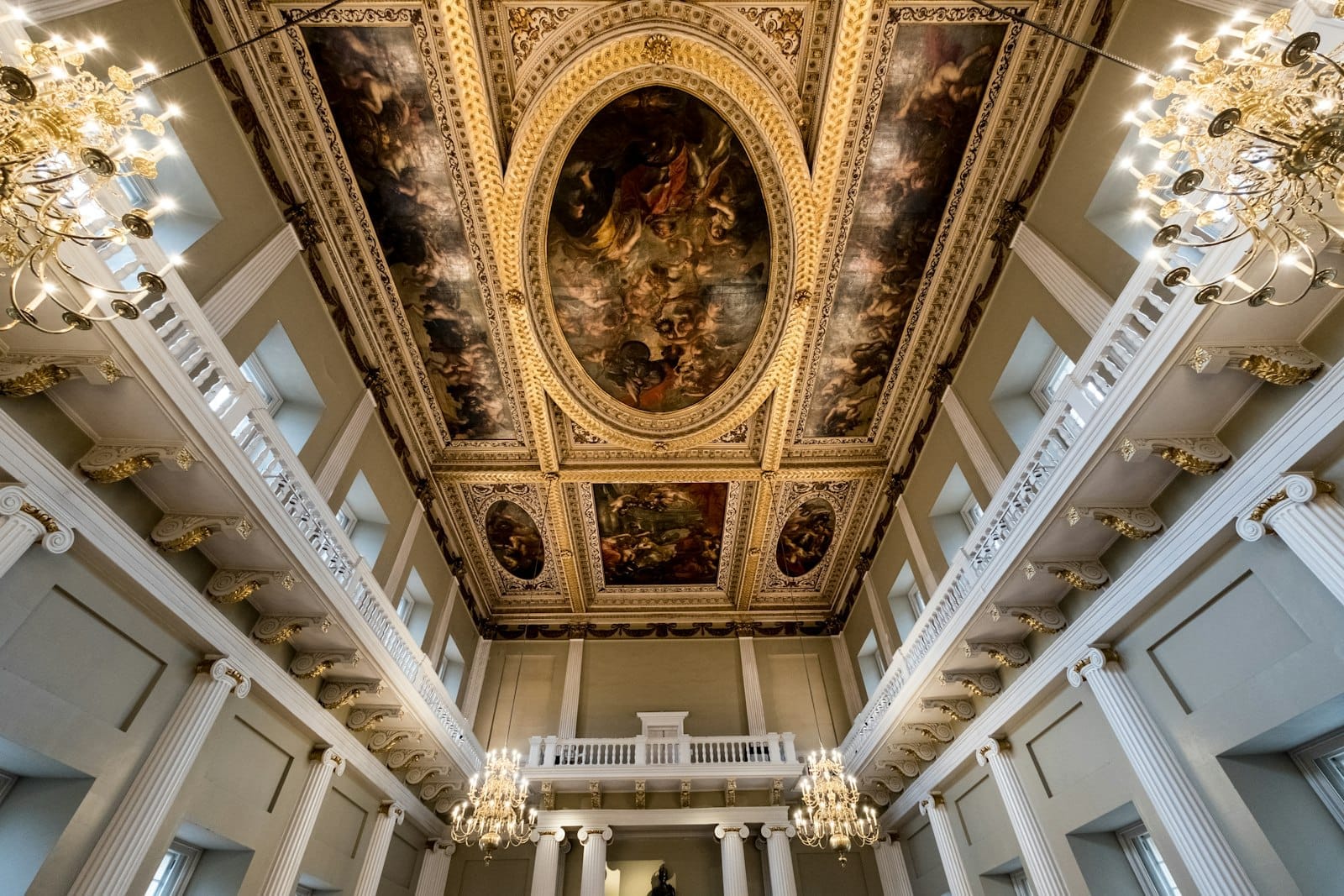Interno del Banqueting House con il suo grandioso soffitto dipinto da Rubens, colonne bianche, dettagli dorati e lampadari ornati.