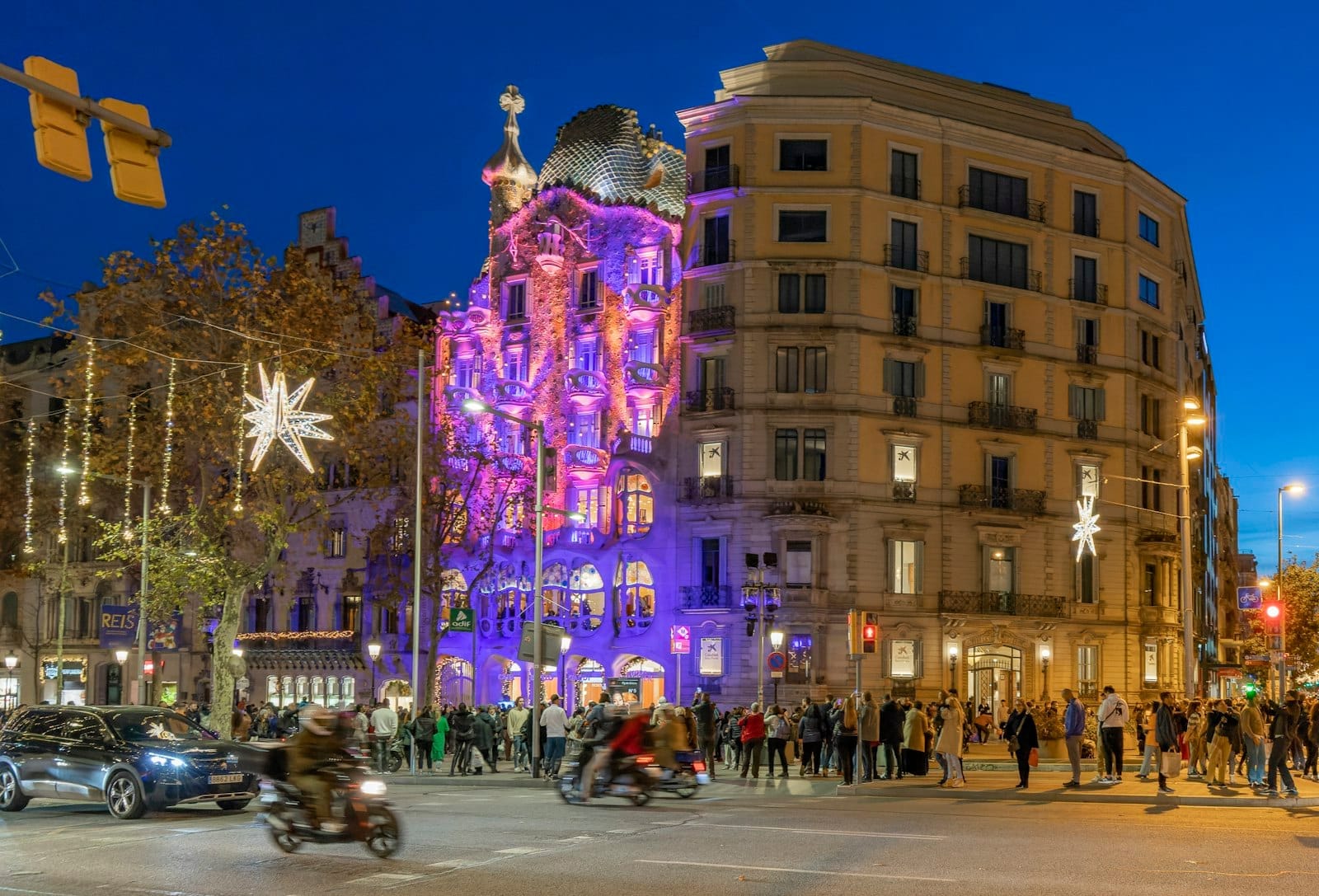 Casa Batlló on Passeig de Gràcia illuminated with colorful lights at night, surrounded by people and festive city life in Barcelona.