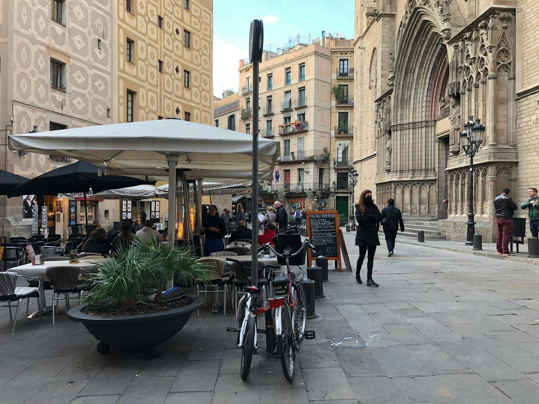 Outdoor cafe with people dining near a Gothic church facade and Barcelona-style apartments in a historic city square.