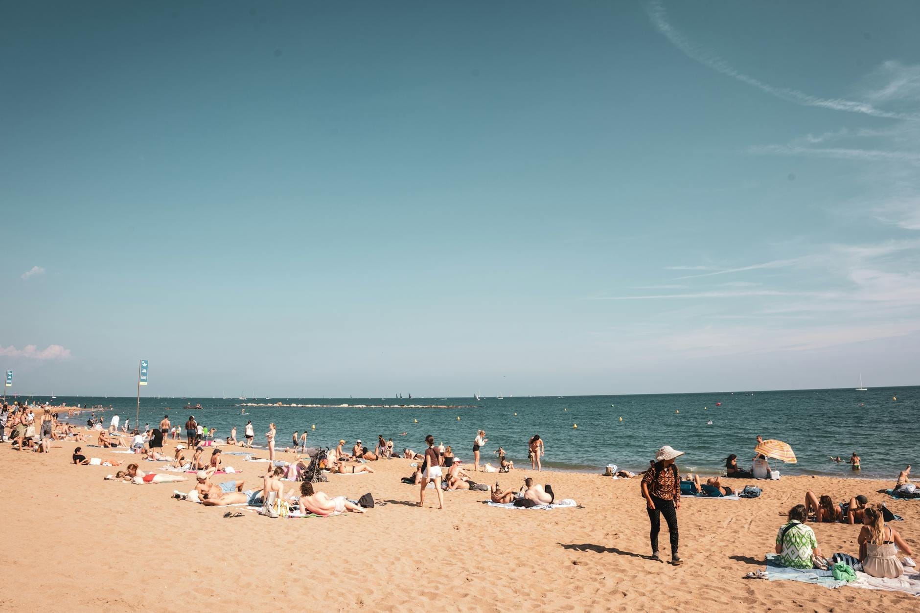 Wide sandy beach with people relaxing and swimming, less crowded with calm sea and open sky, resembling quieter Barcelona coast.
