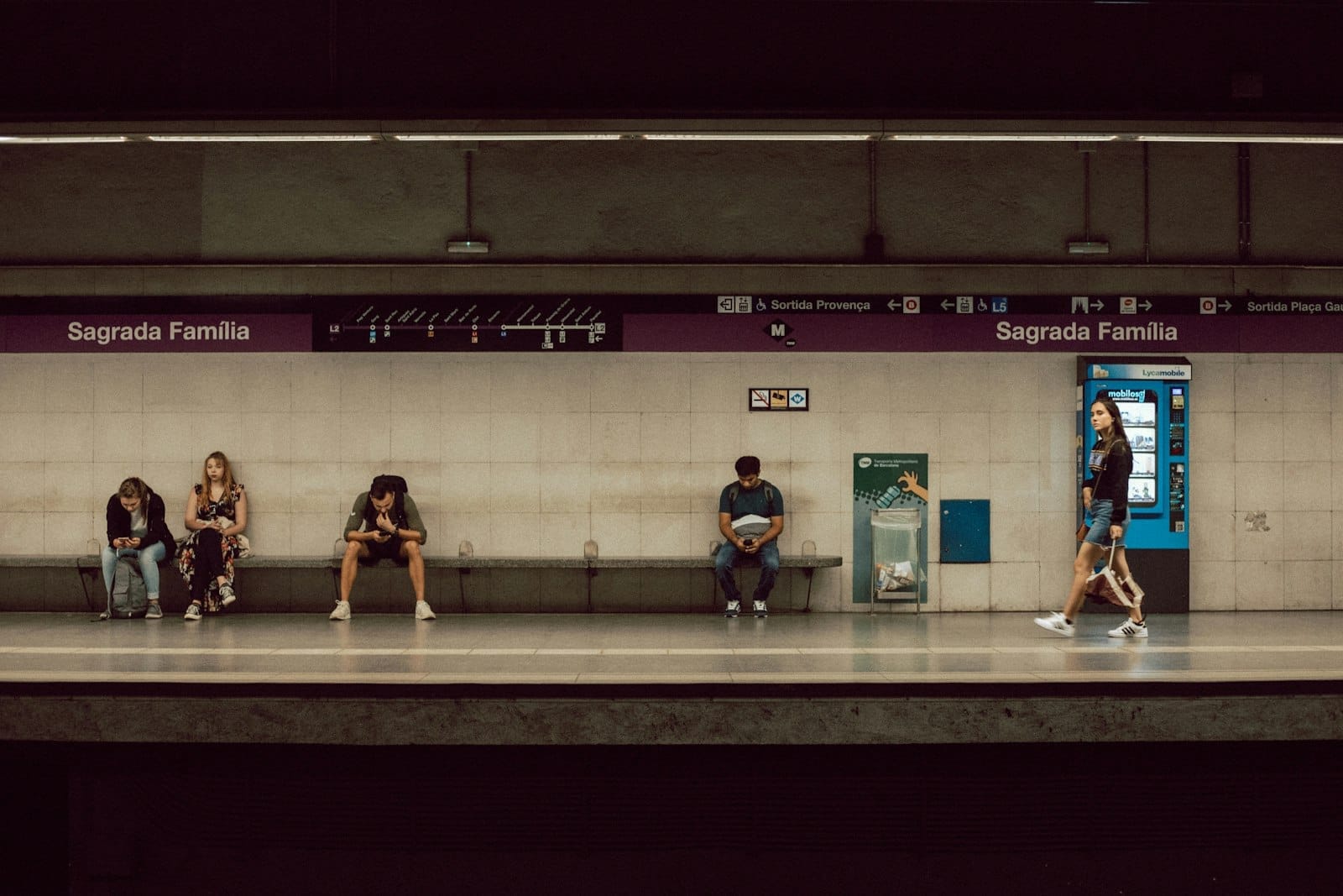 Well-lit Barcelona metro platform at Sagrada Familia station with people waiting and walking, clear signage above the platform.