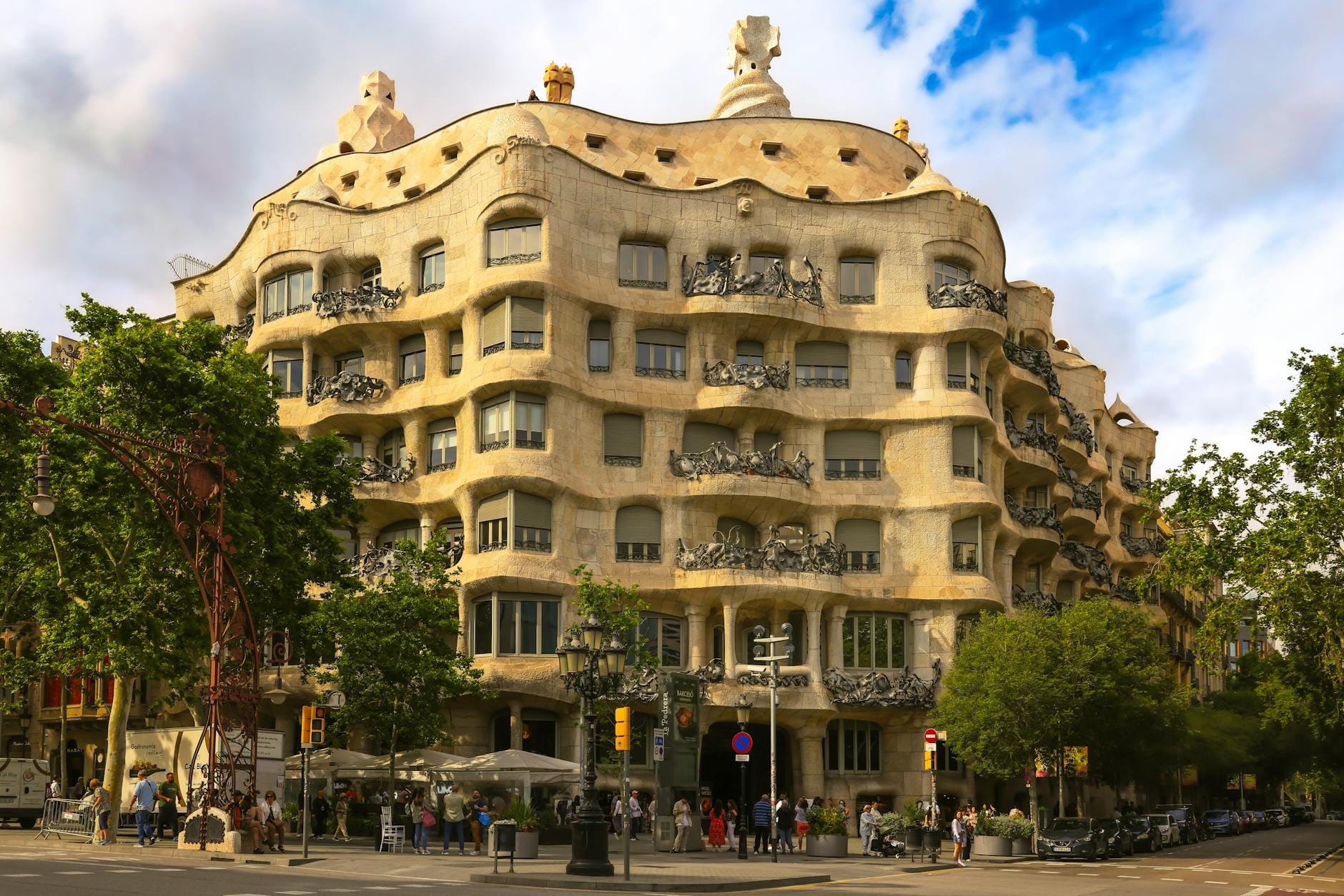 Wide view of Casa Milà (La Pedrera) in Barcelona with people and trees on a sunny day