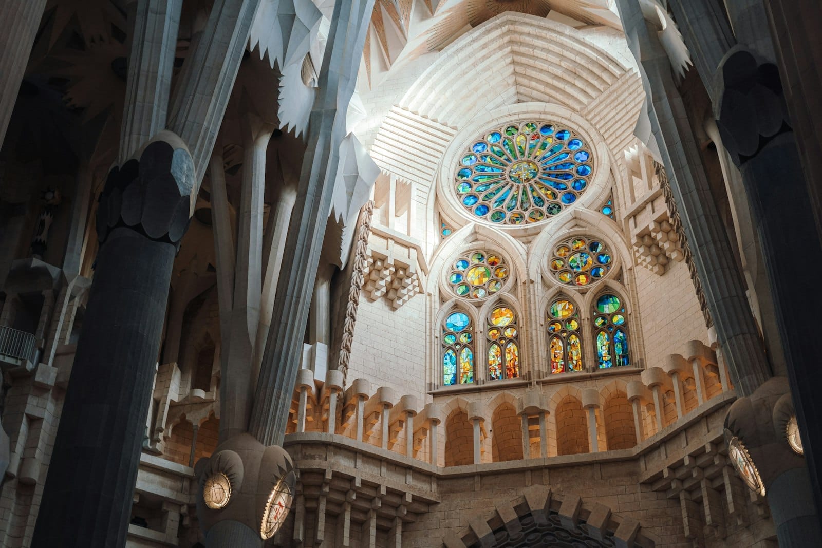 Interior view of Sagrada Família with Gaudí’s organic columns, colorful stained glass windows, and detailed architectural elements illuminated by natural light.
