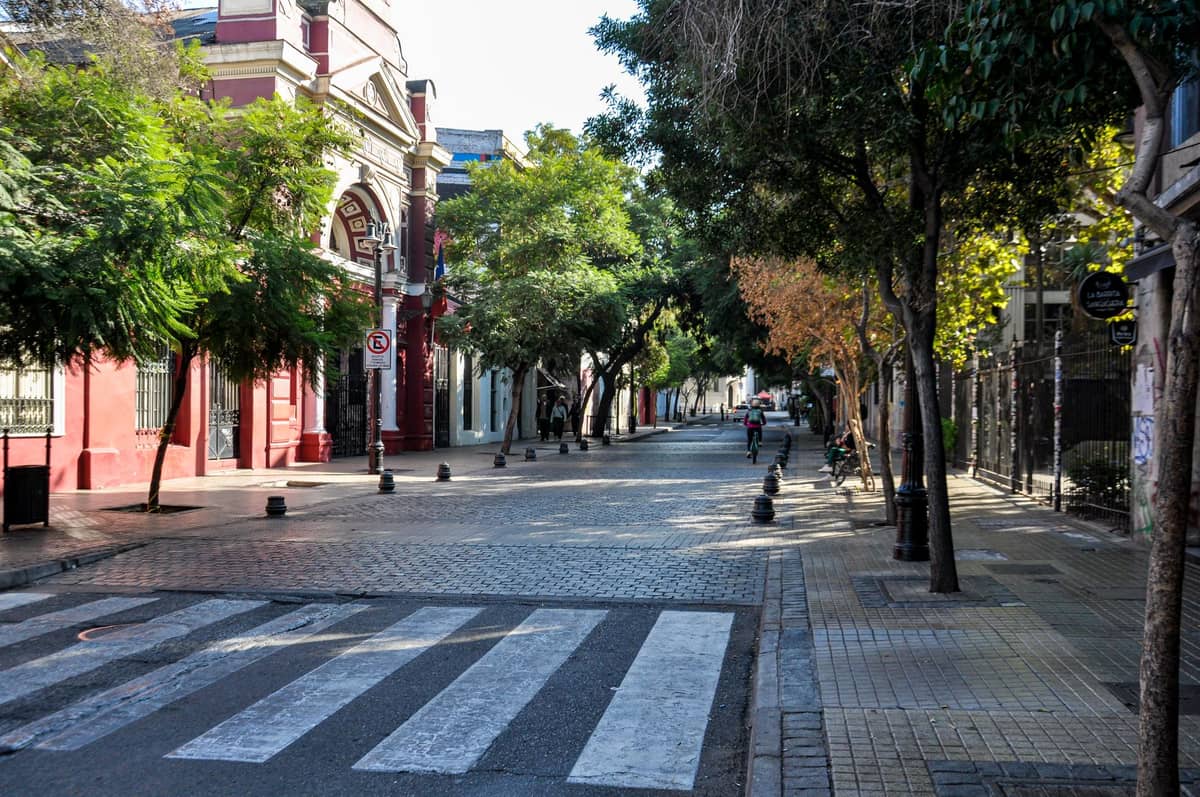 ถนนที่มีต้นไม้ร่มรื่น ปูด้วยหินใน Barrio Sur หรือ Palermo ของมอนเตวิเดโอ รายล้อมด้วยตึกสีสันสดใสและผู้คนเดินเล่นในระยะไกล ท่ามกลางวันแดดดี