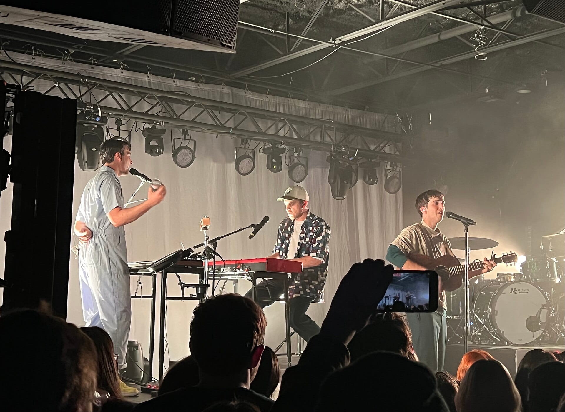 Una banda actúa en el escenario de The Basement East en Nashville, con teclados, guitarra, luces de escenario y un público entusiasta en primer plano.