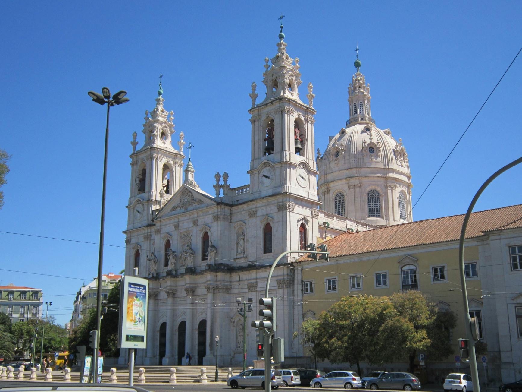 Vista frontale della Basílica da Estrela a Lisbona con cielo azzurro limpido, con i due campanili e la grande cupola della chiesa, tra le strade della città.