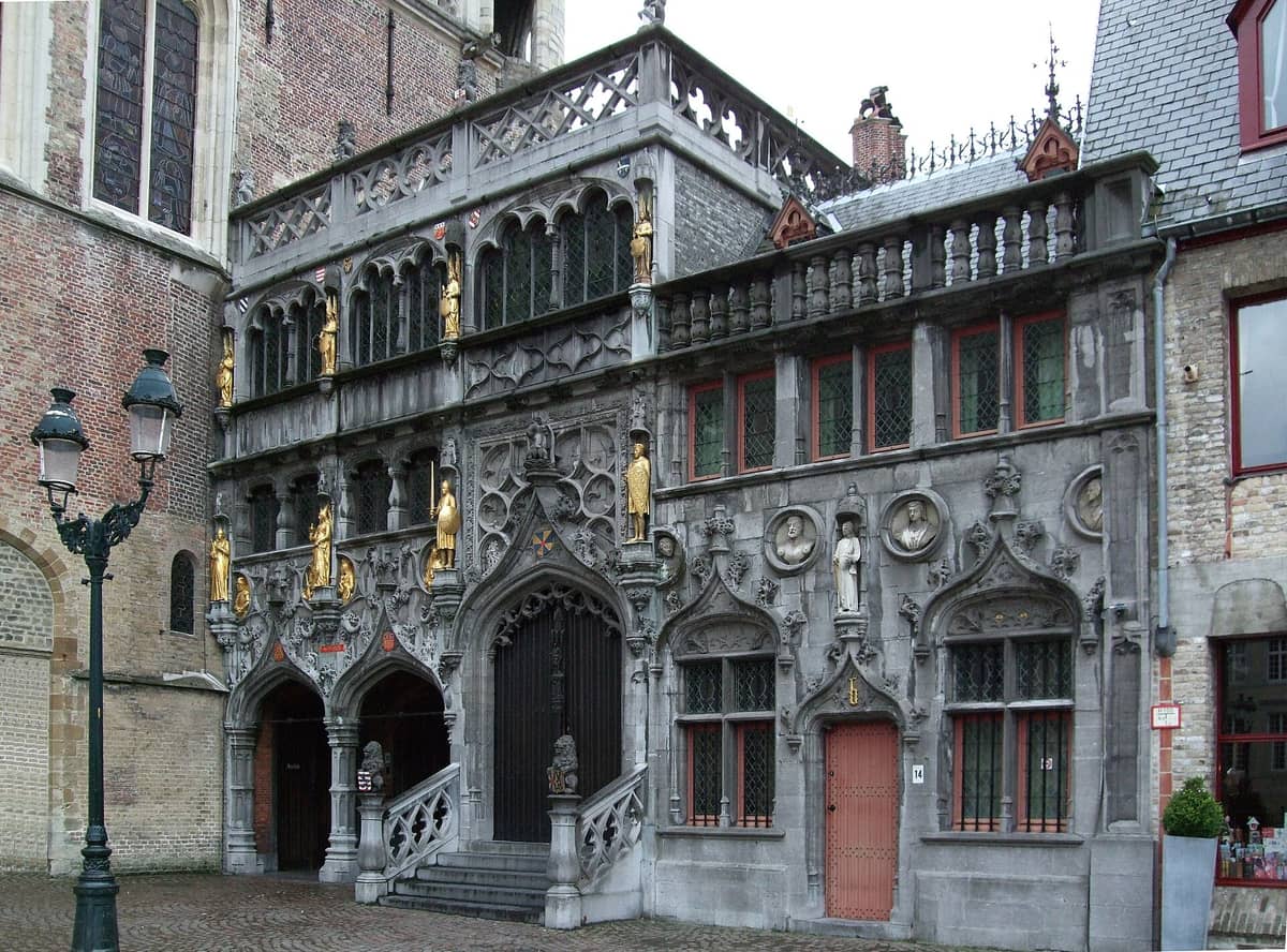 Facade of the Basilica of the Holy Blood in Bruges with ornate Gothic arches, detailed stonework, and golden statues on Burg Square.
