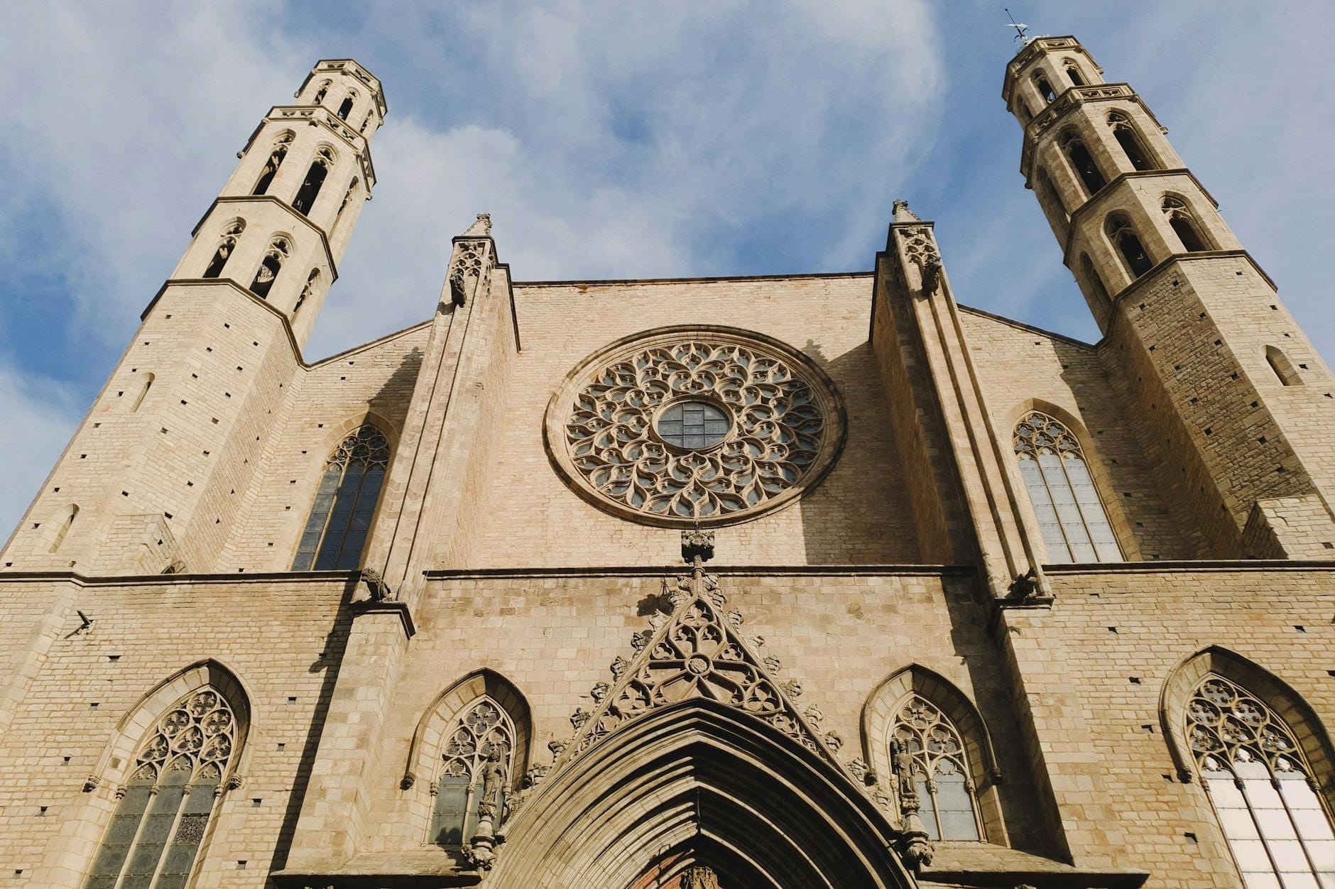 Low-angle view of the Basílica de Santa Maria del Mar's stone facade with large rose window and twin octagonal towers against a blue sky.