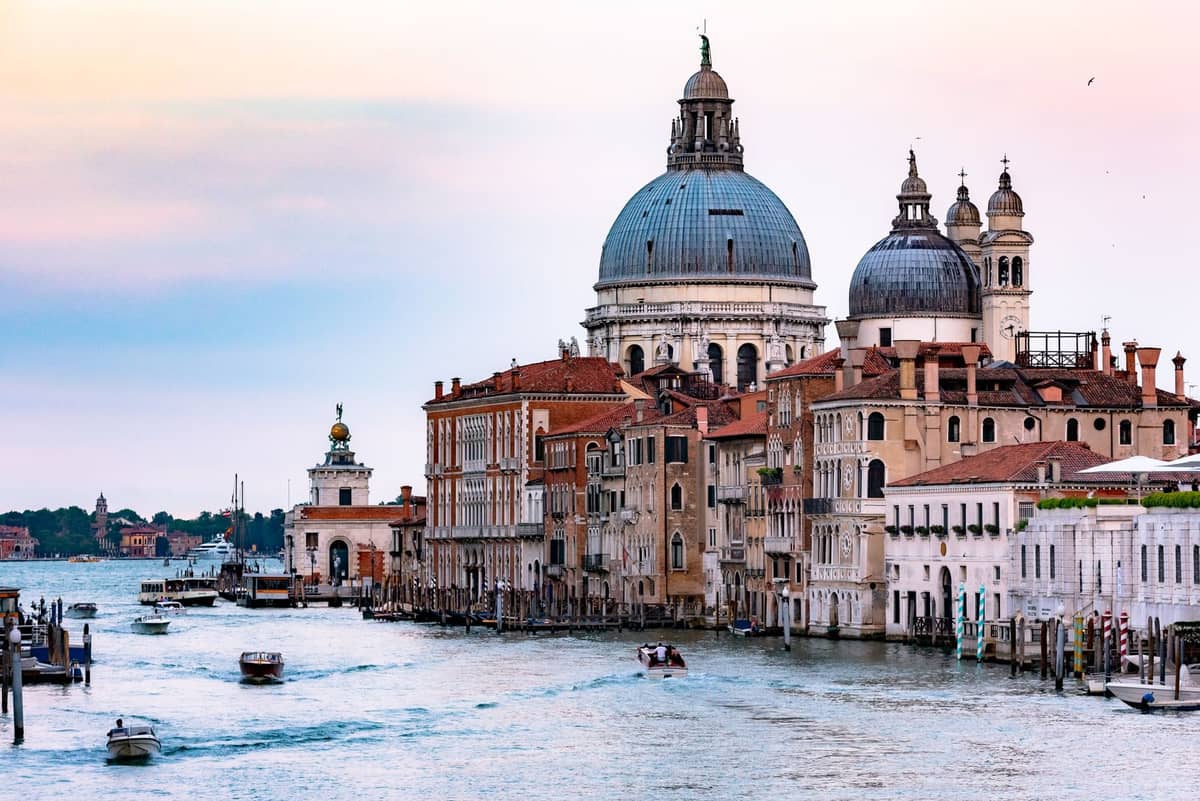 Basilica di Santa Maria della Salute bei Sonnenuntergang, vom Canal Grande aus gesehen, mit Booten und historischen venezianischen Gebäuden am Wasser.
