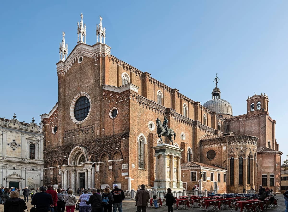 Außenansicht der Basilica dei Santi Giovanni e Paolo in Venedig mit ihrer gotischen Backsteinfront, der Kuppel und dem Reiterstandbild im Vordergrund.
