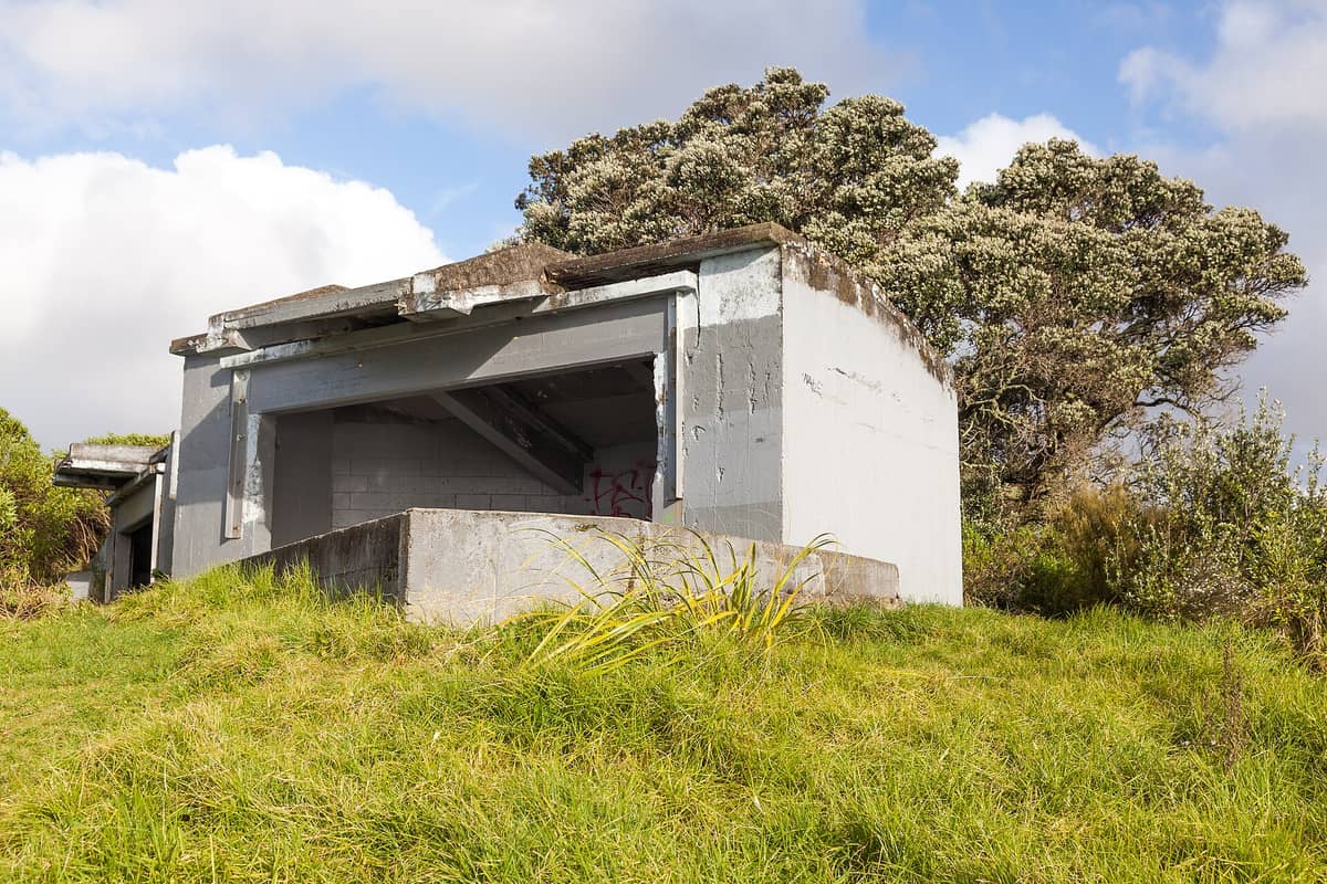 Ein historischer Betonausblick oder Militärbunker am Bastion Point (Takaparawhau), umgeben von Gras und einheimischen Bäumen unter einem bewölkten Himmel.