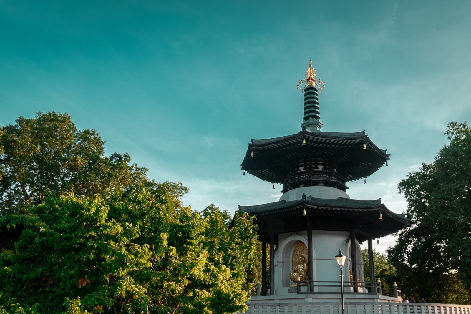 Buddhist Peace Pagoda nel Battersea Park, Londra, circondata da alberi verdi sotto un cielo azzurro limpido con luce solare dorata.