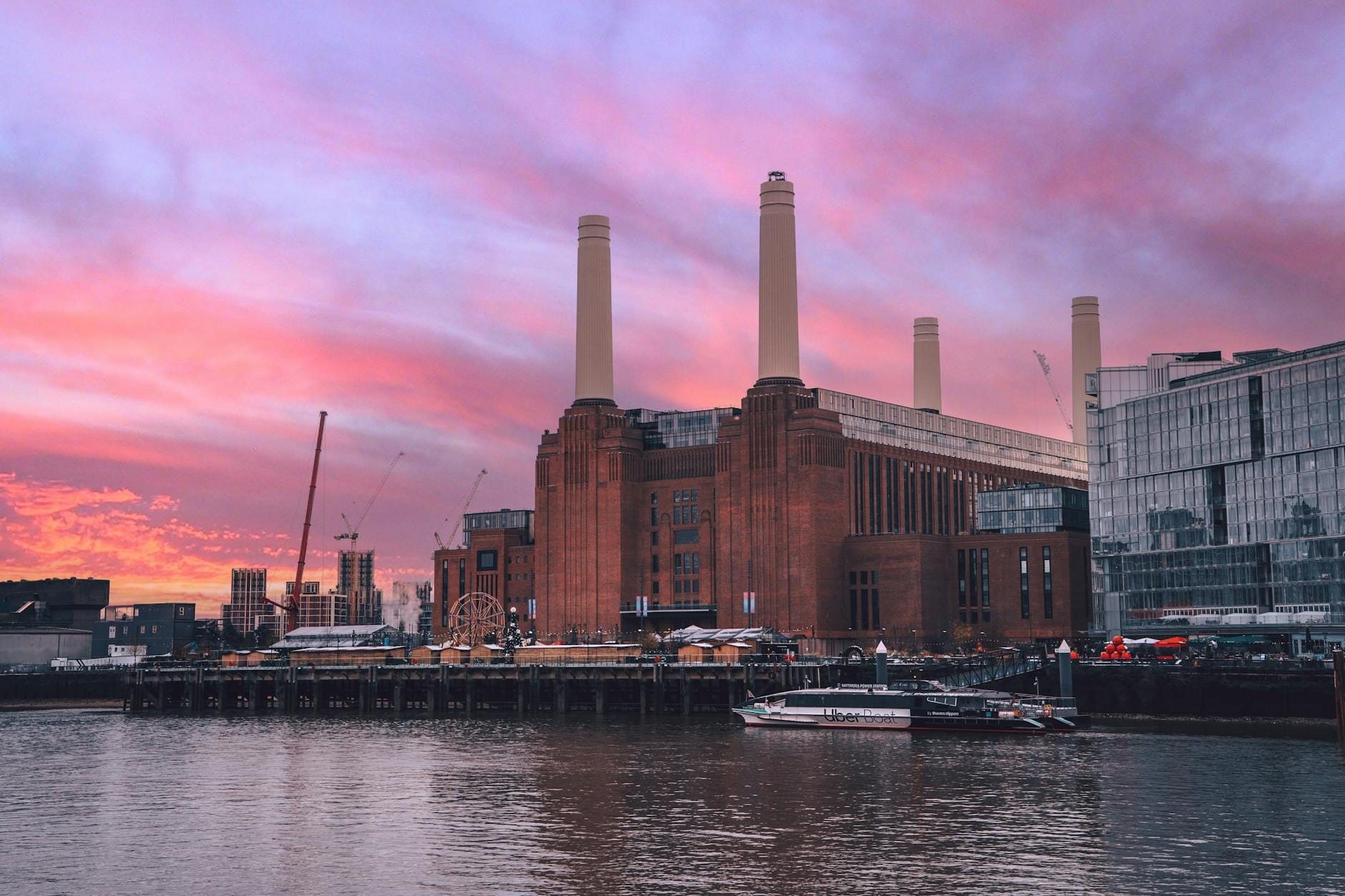Battersea Power Station con le sue iconiche ciminiere vista dall'altra sponda del Tamigi sotto un vivace cielo al tramonto rosa e viola.