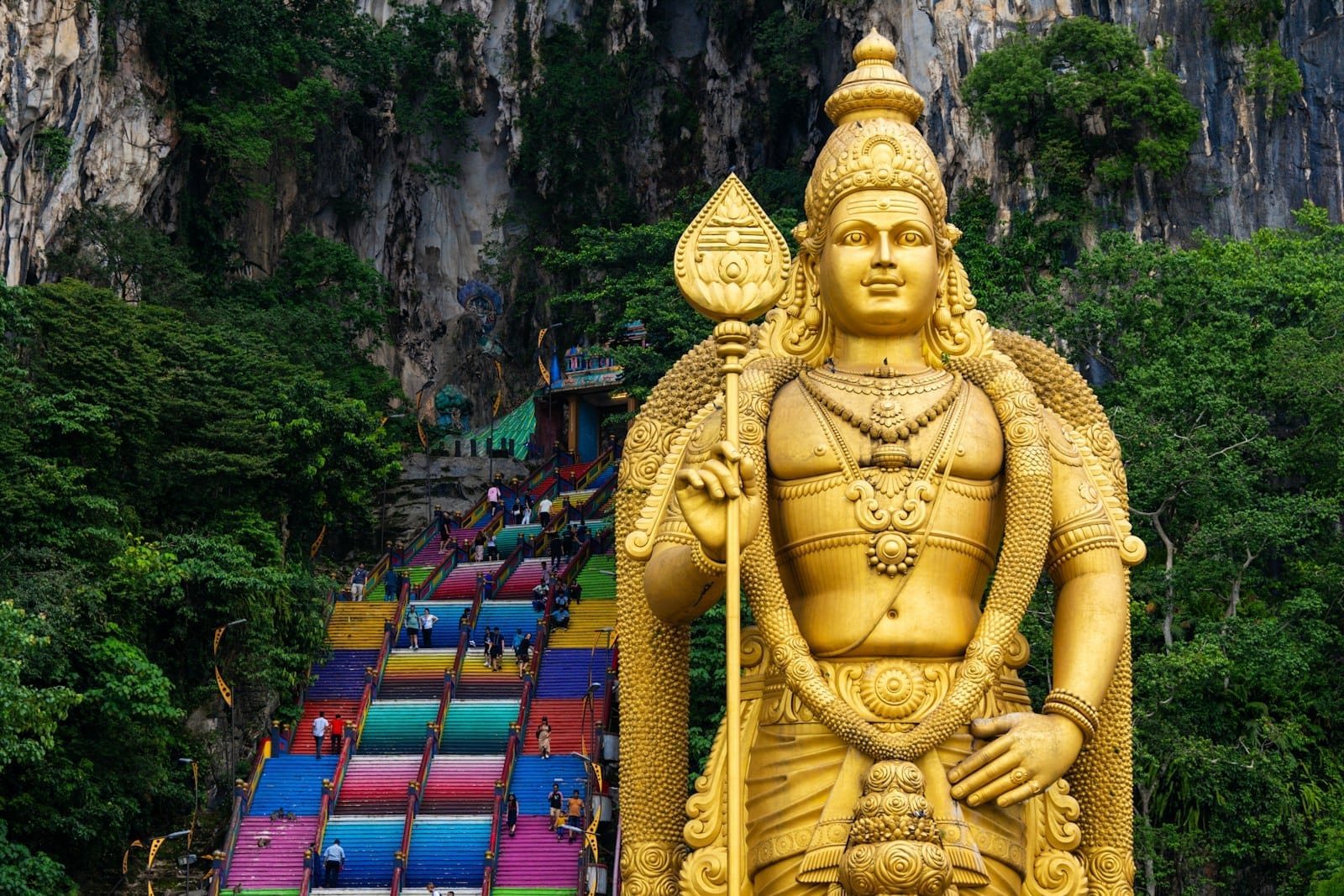 Travelers ascend the iconic rainbow steps at Batu Caves beneath the towering statue, embarking on a colorful journey into Malaysia’s celebrated Hindu temple complex.