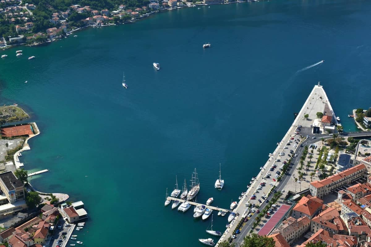 Aerial view of Kotor Marina with several boats docked, adjacent to the Old Town walls and waterfront promenade.