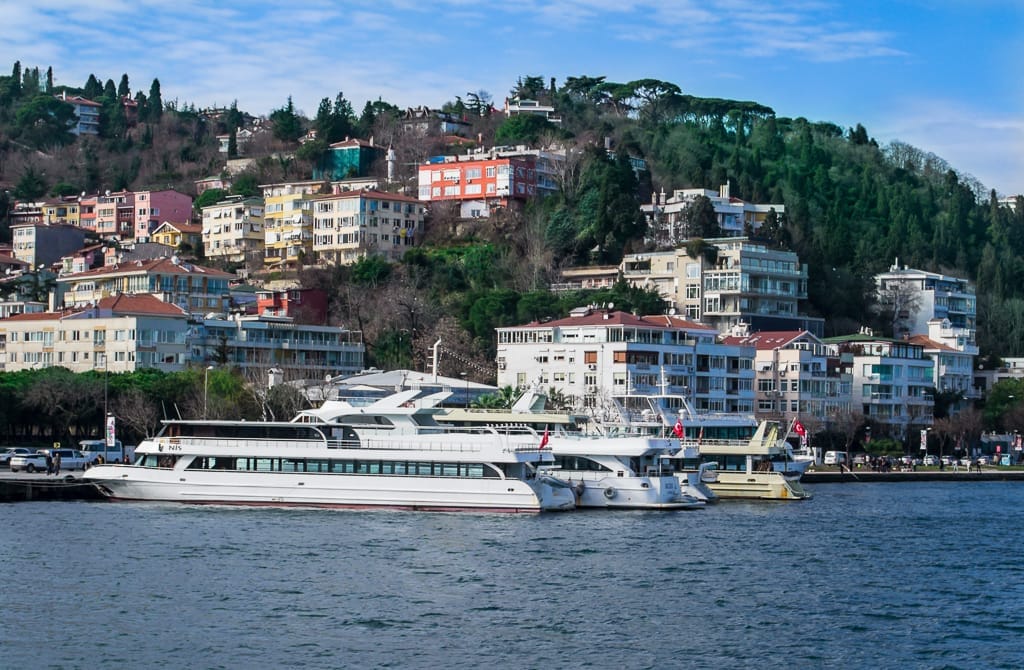 Colorati edifici residenziali e yacht costeggiano la riva del lungomare di Bebek, con rigogliose colline verdi sullo sfondo sul Bosforo di Istanbul.