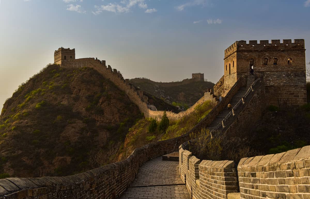 Close-up landscape view of the Great Wall of China winding across green hills with watchtowers under a blue sky, showing a restored section.