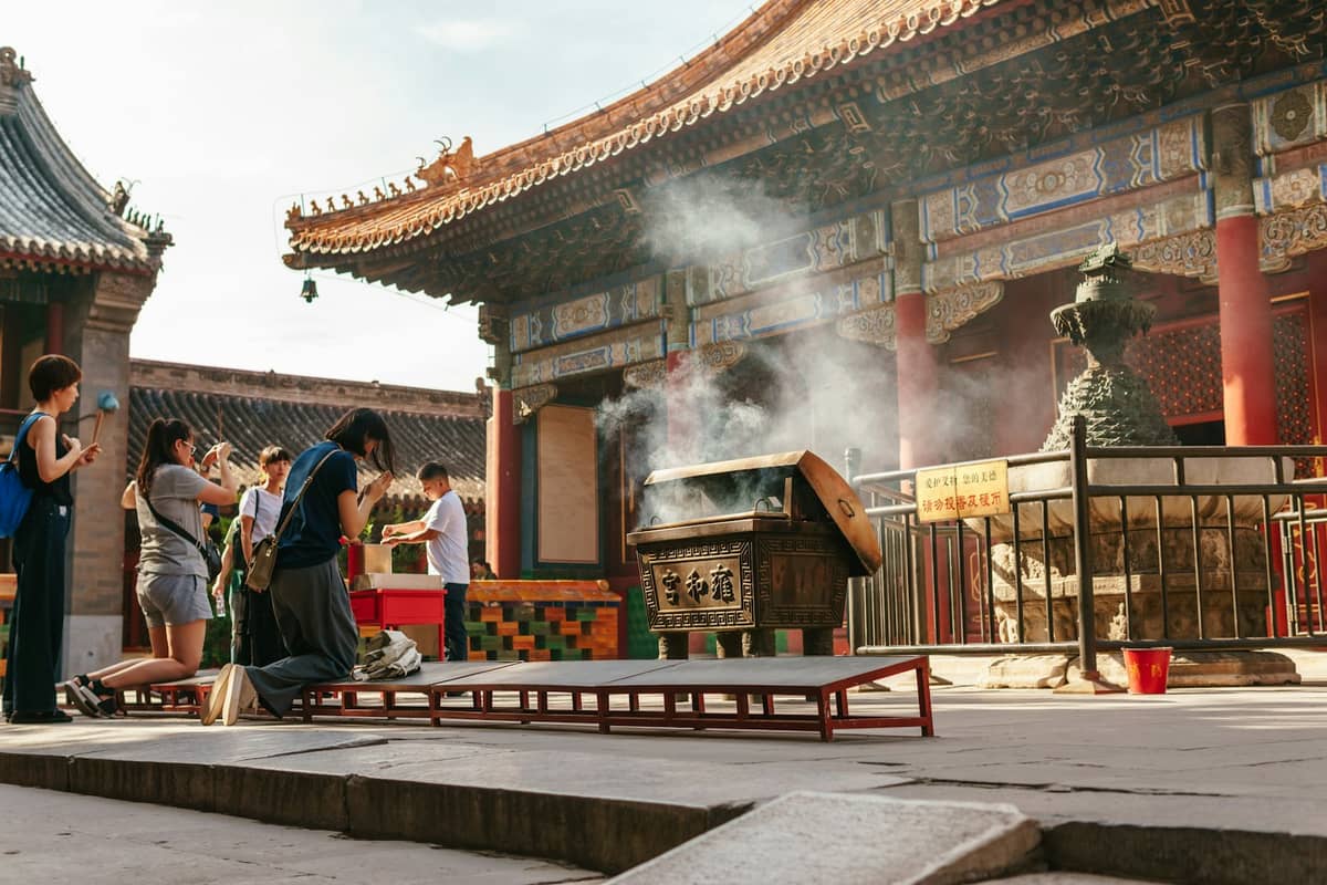 People burning incense and praying in the courtyard of Beijing’s Lama Temple, with smoke rising in front of ornate temple buildings.