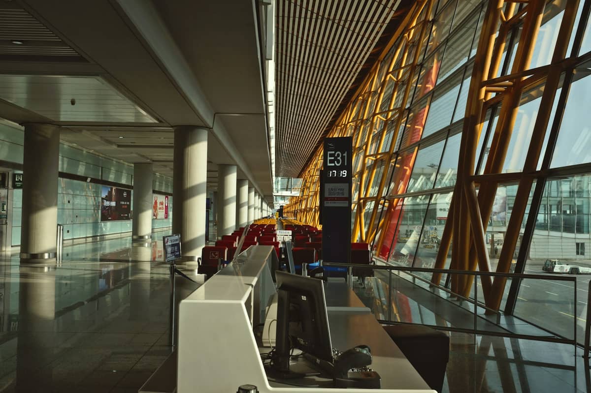 Innenansicht des Terminals am Beijing Capital International Airport mit markanten gelben Säulen, Check-in-Schaltern und großen Glasfenstern mit Blick auf das Rollfeld.