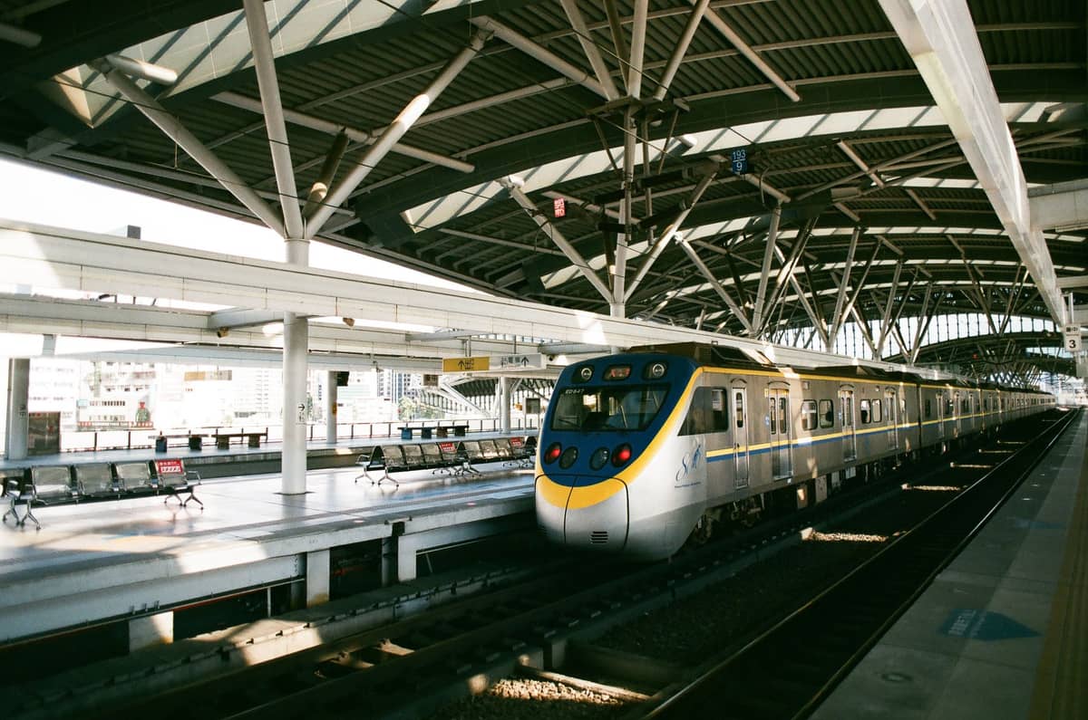 Un moderno tren expreso del aeropuerto en un andén bajo una gran marquesina de acero, que sugiere una conexión ferroviaria directa al aeropuerto.