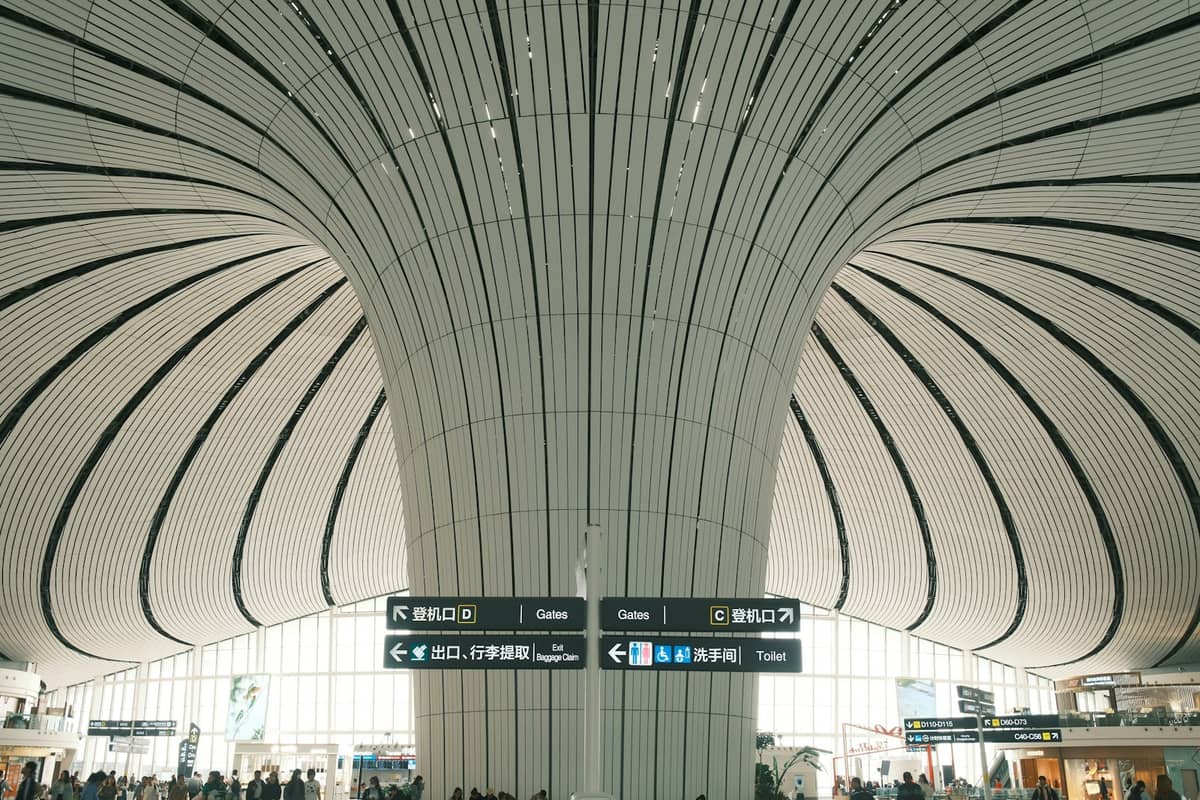 Vista amplia del interior de la sala principal futurista del Aeropuerto Internacional de Beijing Daxing, con techo curvo y señales del aeropuerto.