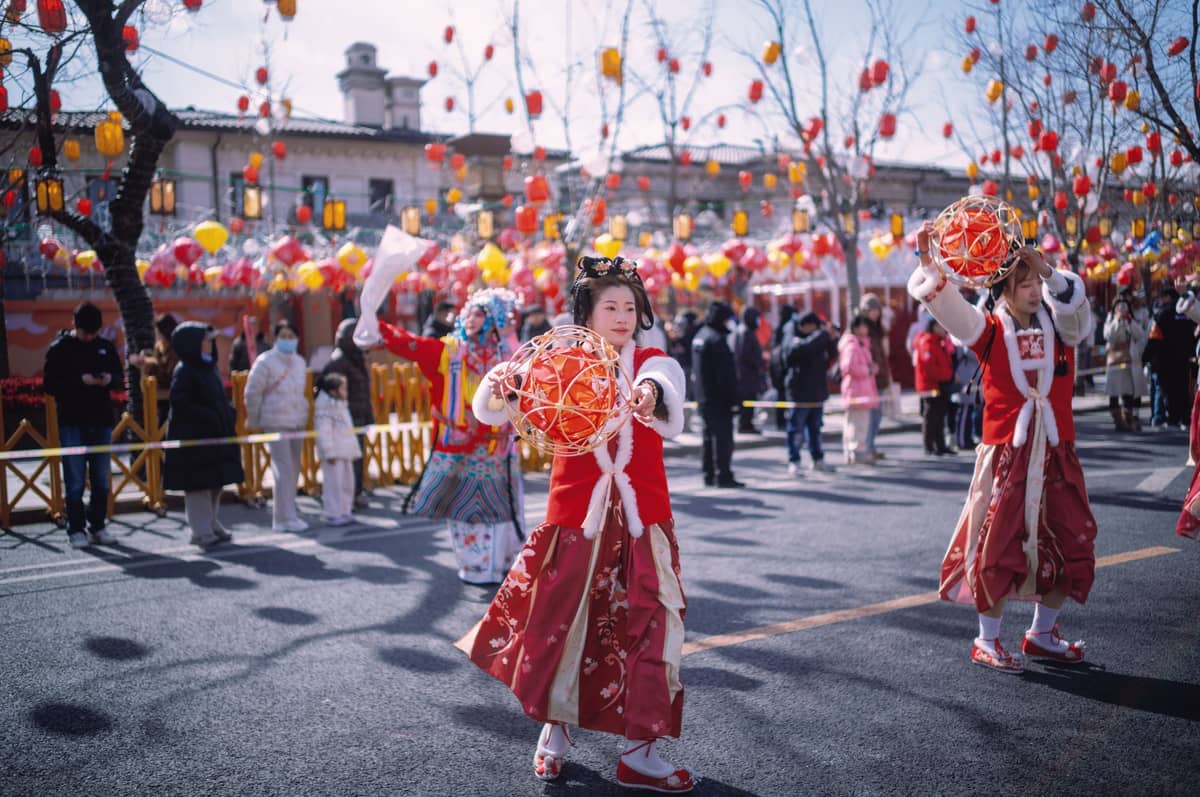 Traditionelle Tänzer in festlichen Kostümen bei einem Pekinger Tempelmarkt zum chinesischen Neujahr, mit Menschenmassen, Laternen und Dekorationen im Hintergrund.