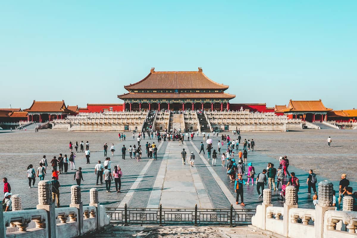 Weitläufige Ansicht der Haupthalle und des großen Innenhofs der Verbotenen Stadt in Peking mit zahlreichen Besuchern unter einem klaren blauen Himmel.