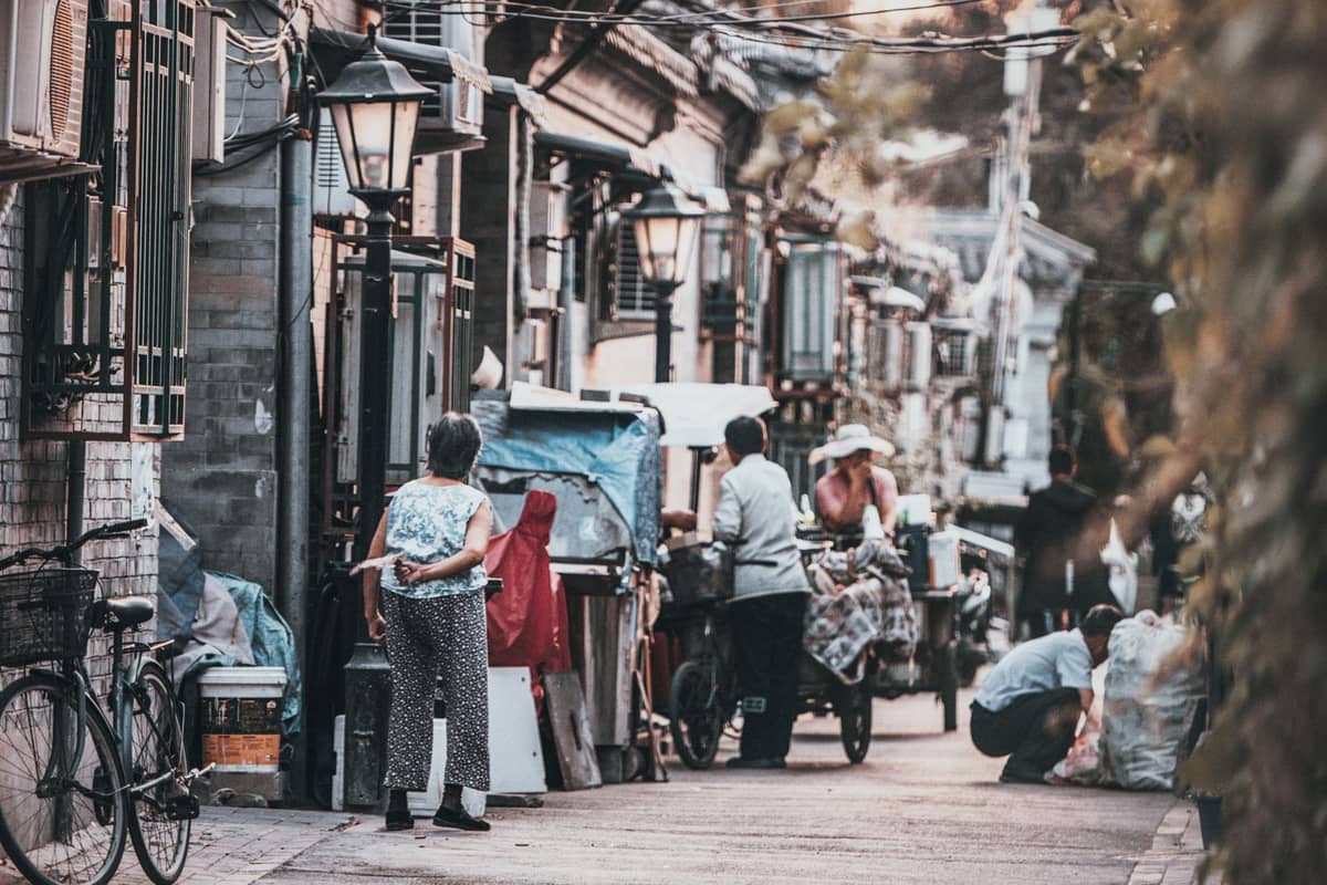 Enge Hutong-Gasse in Peking, gesäumt von alten Backsteinhäusern, Einheimischen zu Fuß und geparkten Fahrrädern, die das Alltagsleben in einem Wohnviertel einfangen.