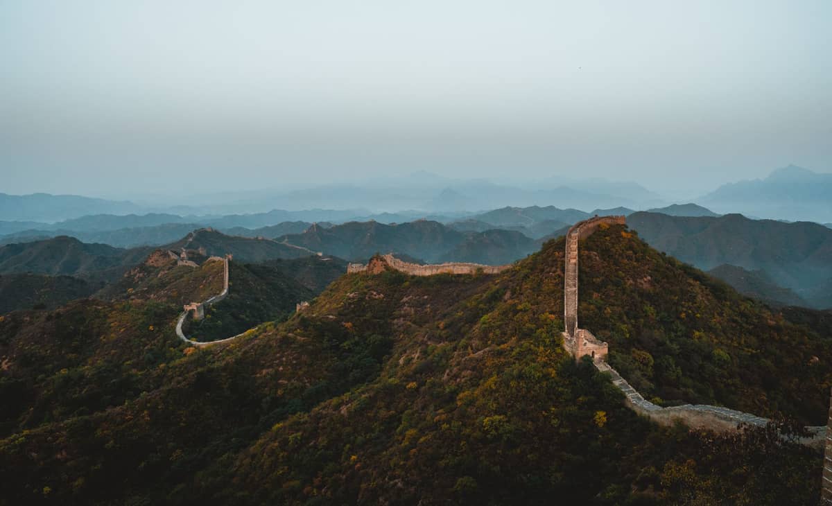Eine weitläufige Landschaftsansicht der Chinesischen Mauer, die sich unter einem klaren Himmel in der Nähe von Beijing über grüne Hügel schlängelt.