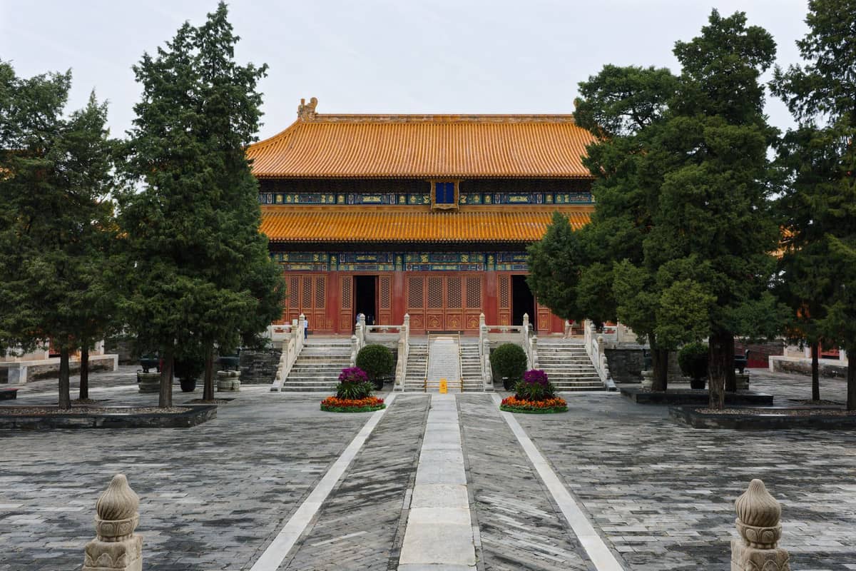 Traditioneller chinesischer Tempel in Beijing mit orangefarbenem Ziegeldach, roten Säulen und einem ruhigen Steinhof, umgeben von grünen Bäumen.