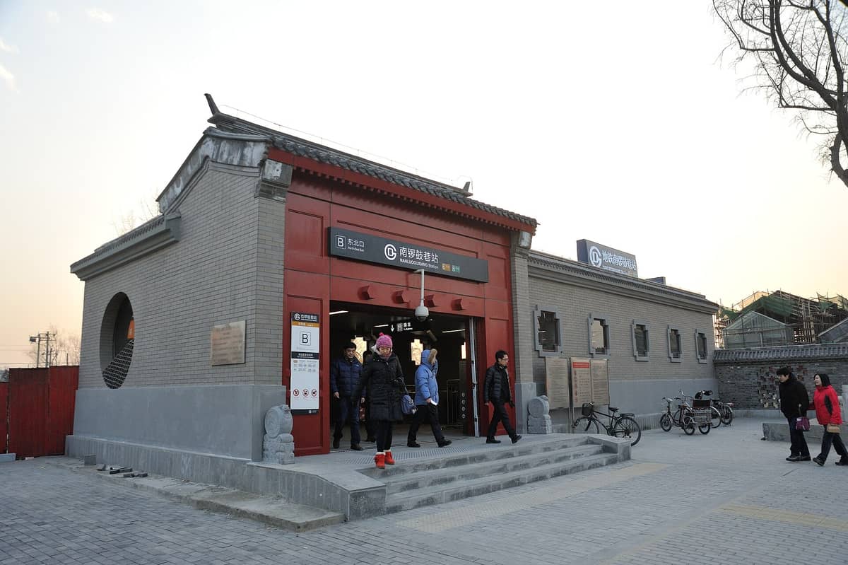Menschen verlassen die Station Nanluoguxiang der Beijing U-Bahn, mit traditionellen grauen Ziegeln und einem roten Toreingang, in der Nähe der Hutong-Gebiete.