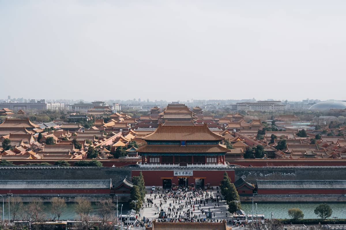 Weiter, klarer Blick auf den Haupteingang und die goldenen Dächer der Verbotenen Stadt, belebt von Besuchern, vor der Skyline von Beijing.
