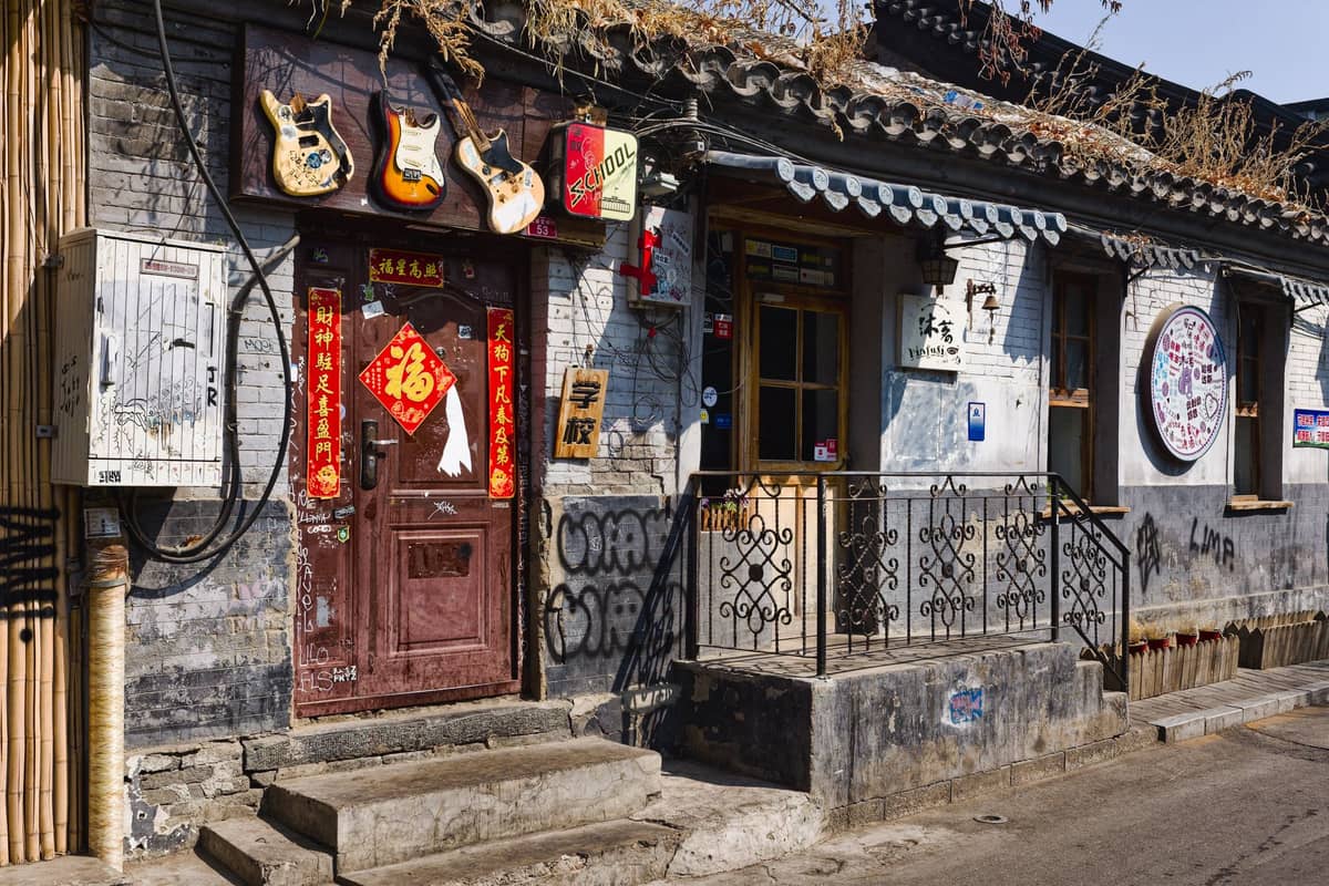 Straßenansicht einer Hutong-Bar in Beijing mit Gitarren über der Tür, chinesischen Laternen und dekorativen Elementen an einer alten Backsteinfront.
