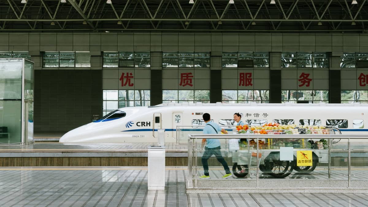 Seitenansicht eines modernen CRH-Hochgeschwindigkeitszuges an einem chinesischen Bahnhof mit Fahrgästen, die auf dem Bahnsteig gehen.