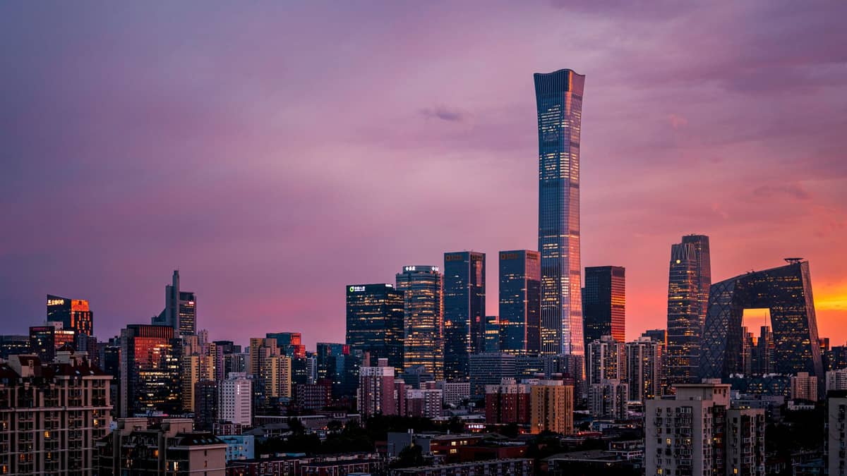 Beijing modern skyline at sunset featuring China Zun tower, CCTV Headquarters, and illuminated cityscape under a purple sky.