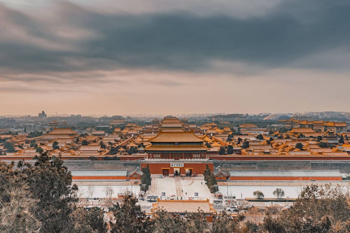 Weitläufige Vogelperspektive auf die Verbotene Stadt in Peking – goldene Kaiserdächer erstrecken sich unter dramatischem Himmel in die Ferne.