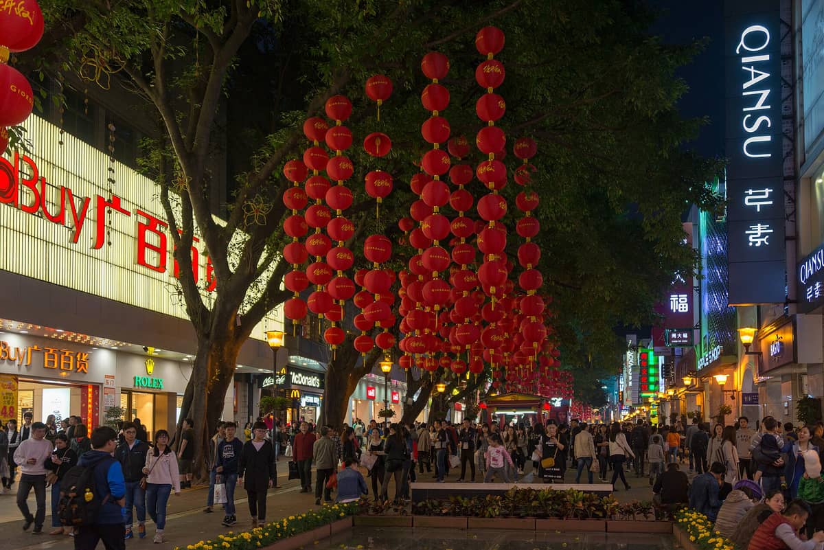 Night scene of Beijing Road Pedestrian Street in Guangzhou, featuring crowds, bright neon signs, red lanterns overhead, and lively storefronts.
