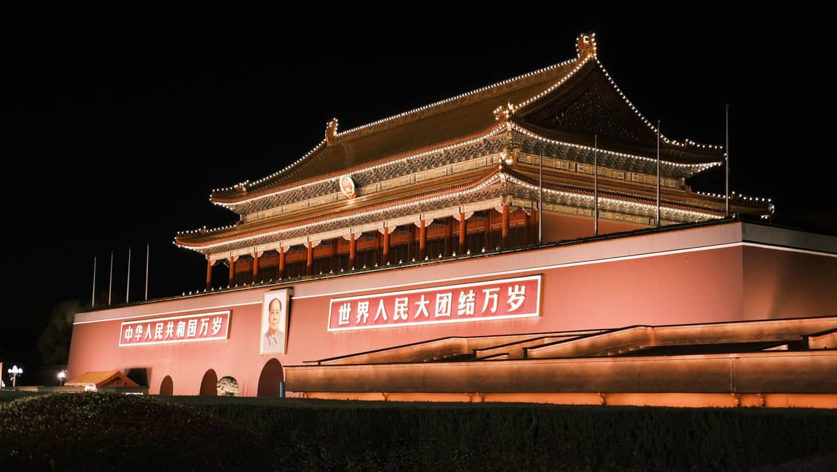 Nächtliche Ansicht des Tiananmen-Tors in Peking, hell beleuchtet mit dem bekannten Porträt und großen Bannern – das Wahrzeichen des Stadtzentrums.