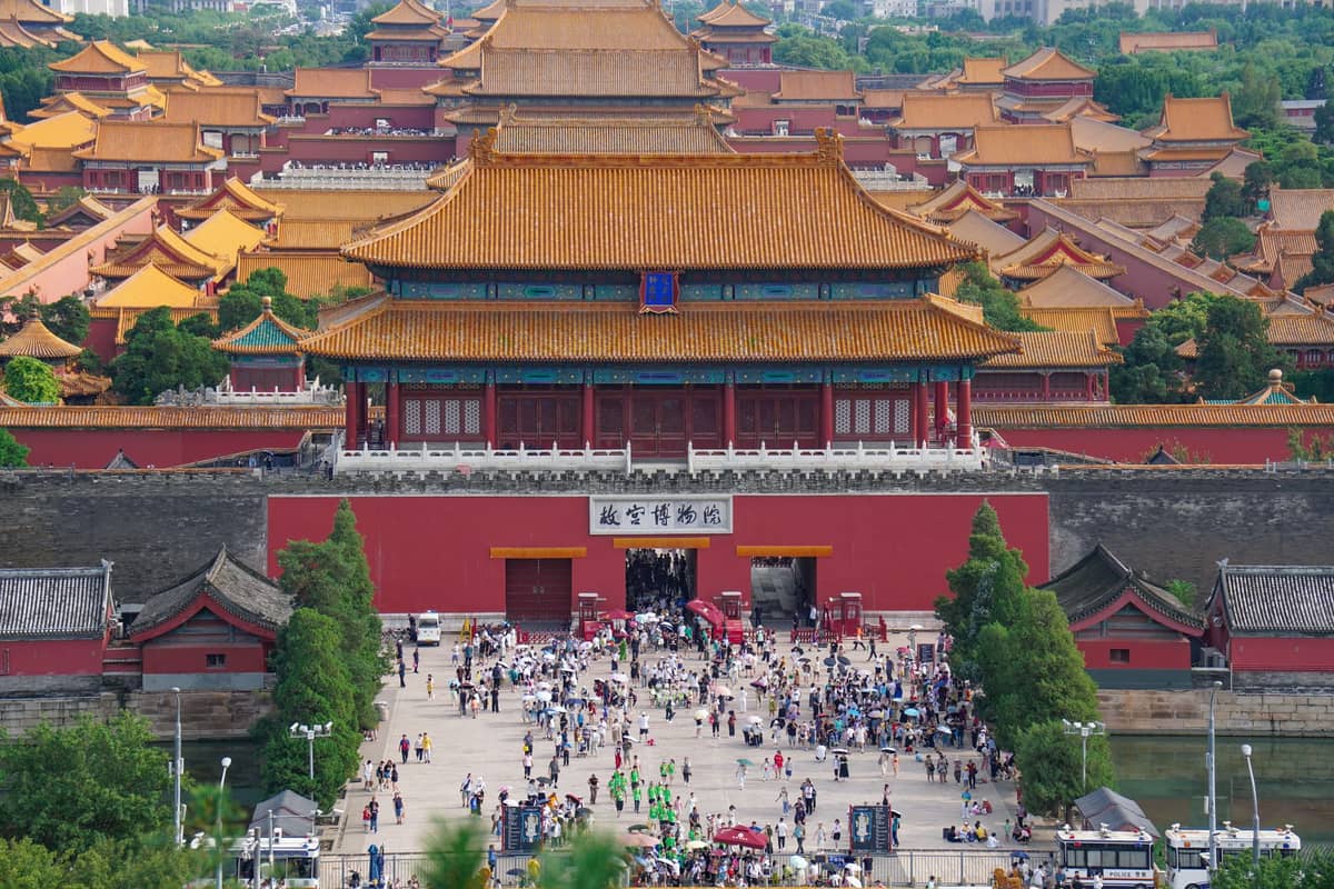 Menschenmengen versammeln sich am Eingang zur Verbotenen Stadt in Beijing mit ihren ikonischen goldenen Dächern und dem weitläufigen Palastkomplex, der sich in die Ferne erstreckt.